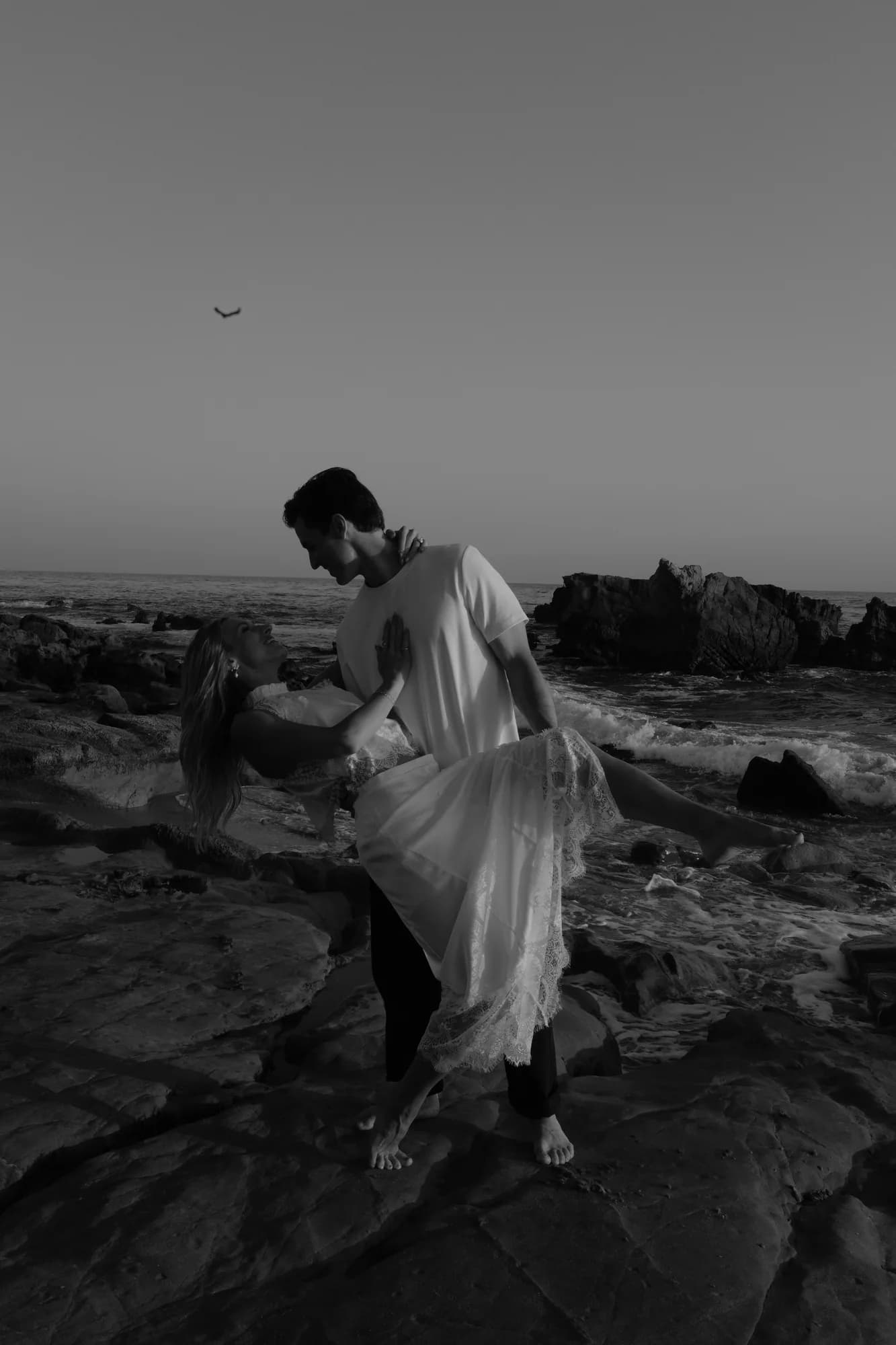 Man dipping his partner on a rocky stretch of the Southern California coast, black and white
