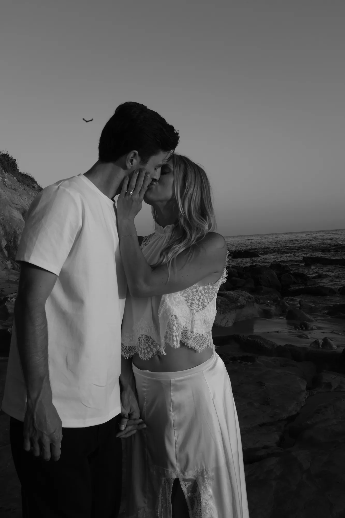 Black and white photo of a couple sharing a kiss on the Orange County coast at dusk