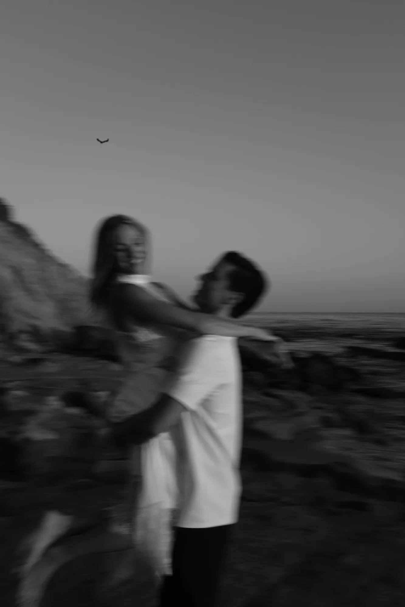 Couple laughing as he lifts her off the ground at the beach, black and white couples session