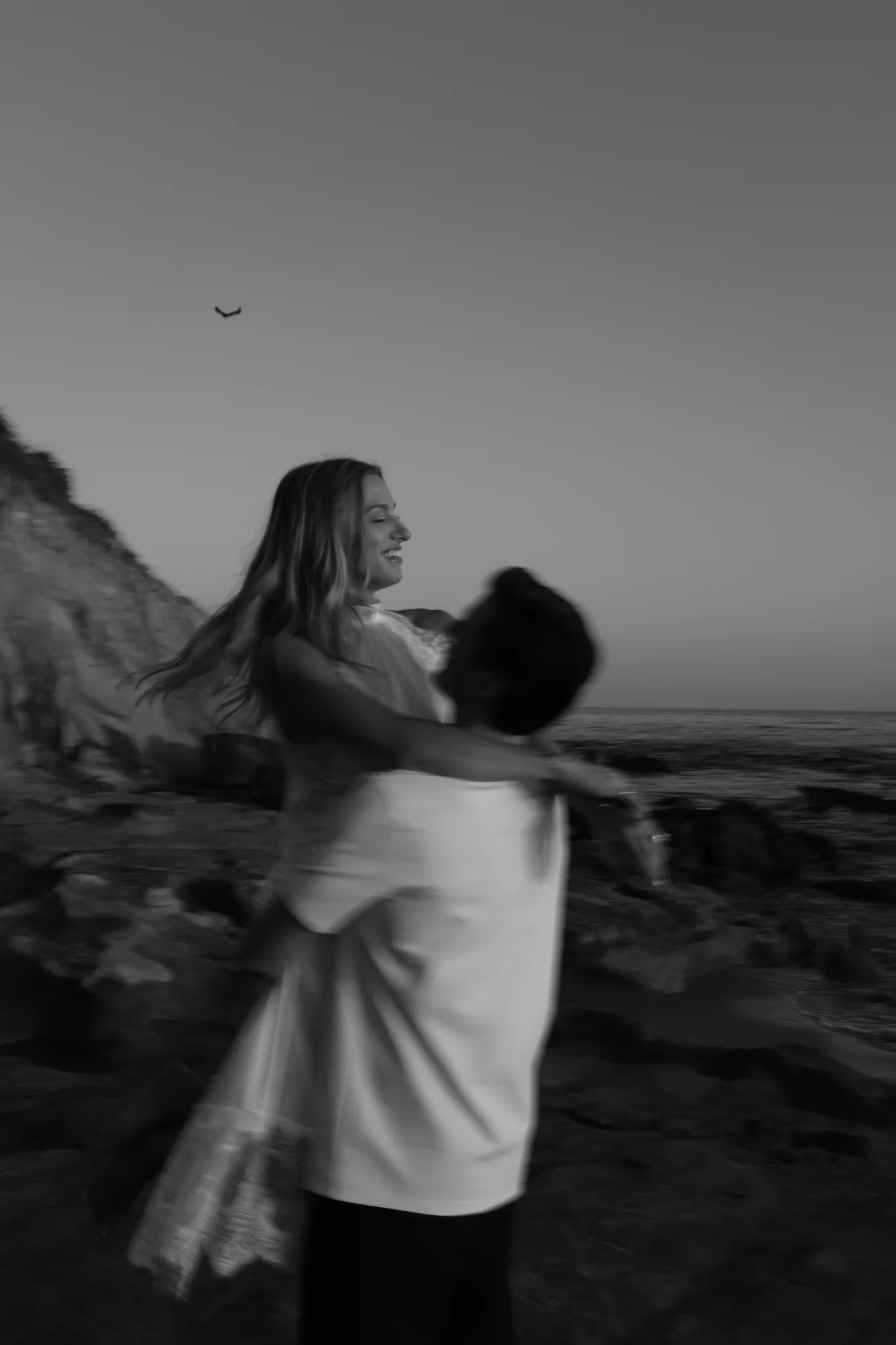 Man lifting his fiancee into the air during an engagement session on the beach, black and white