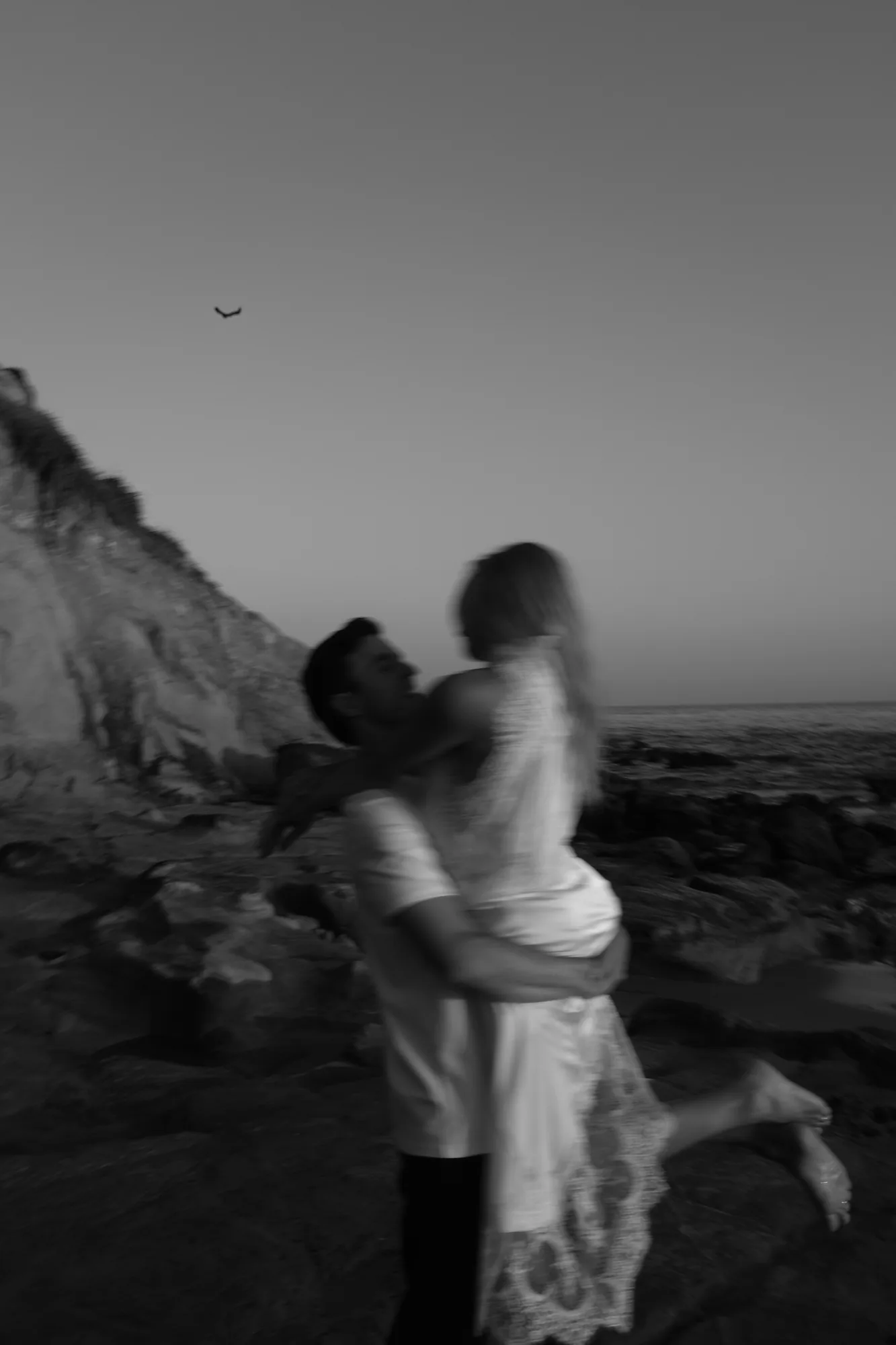 Couple embracing mid-spin in front of a coastal bluff during an engagement session