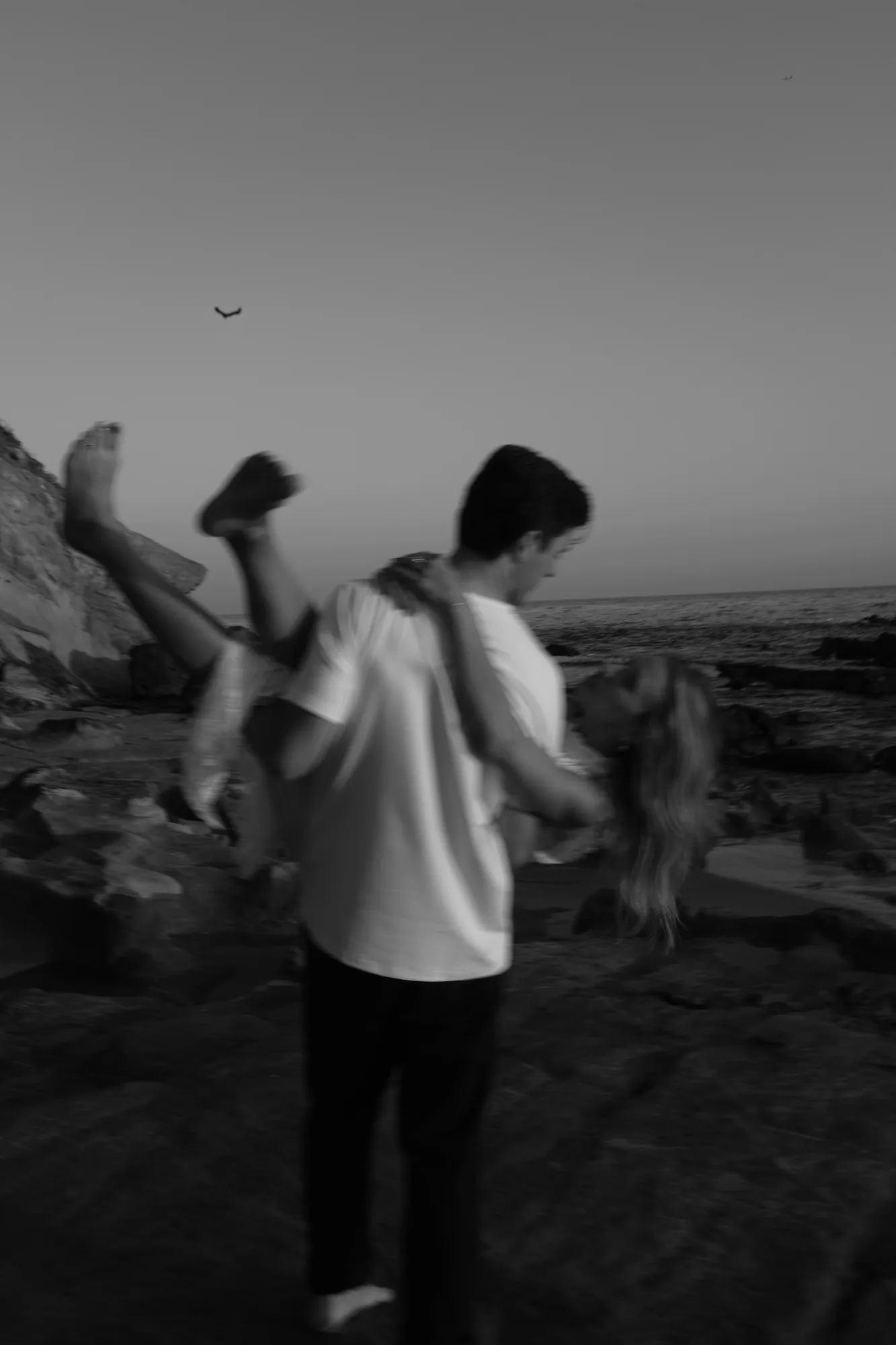 Playful moment of a man carrying his partner on the beach, black and white couples session