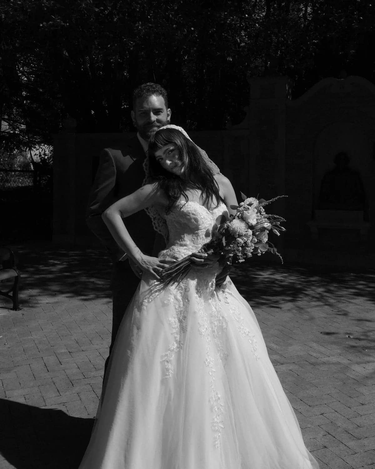 Black and white portrait of a bride holding her bouquet with her groom behind her