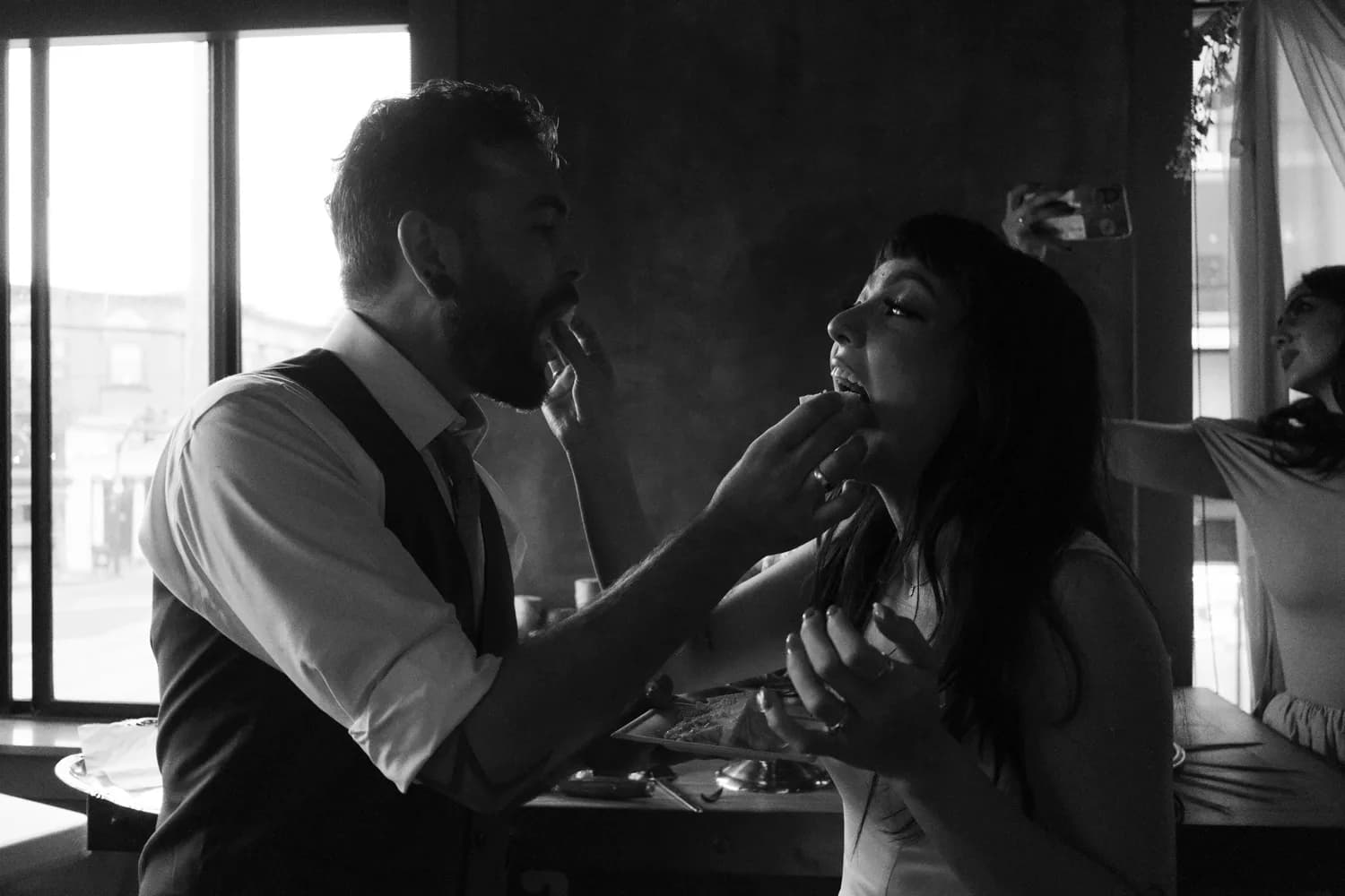 Groom feeding his bride a bite of cake at their reception, black and white