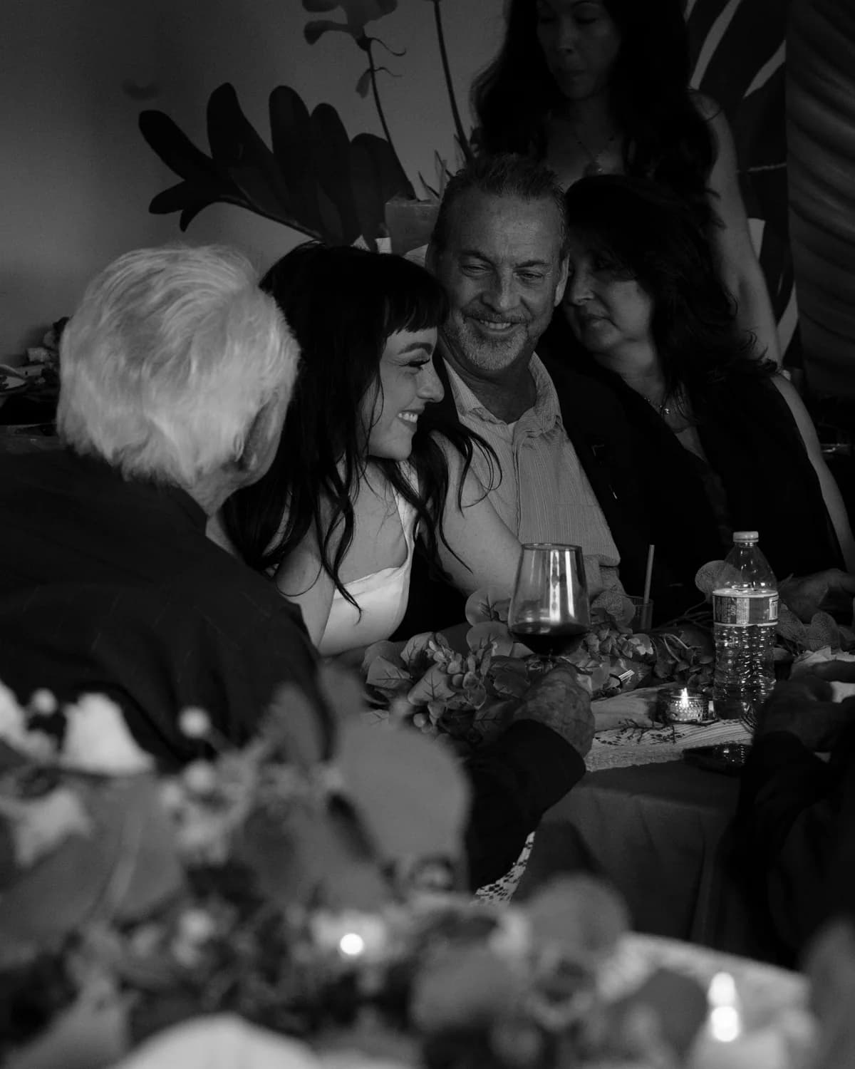 Guests laughing together around a candlelit dinner table, black and white
