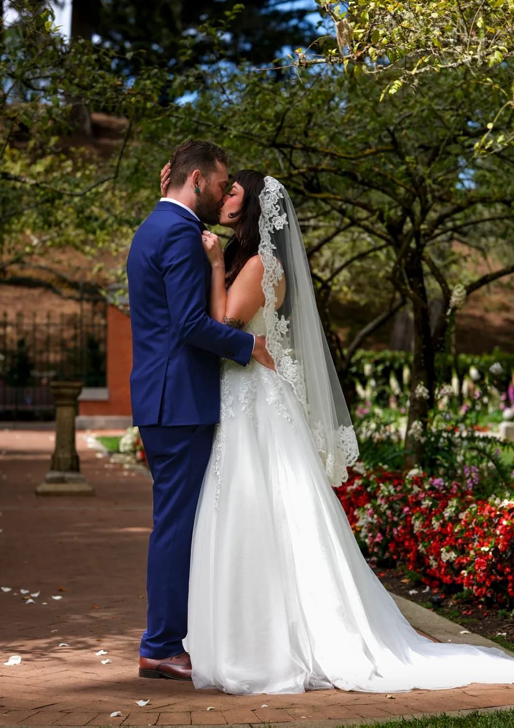 Bride and groom embracing on a brick garden path surrounded by flowers