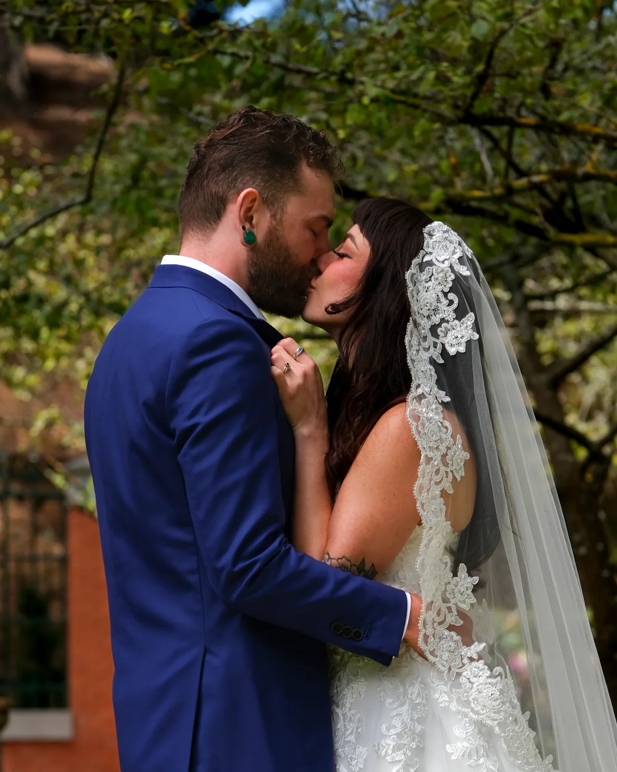 Bride and groom kissing under a lace veil during an outdoor ceremony