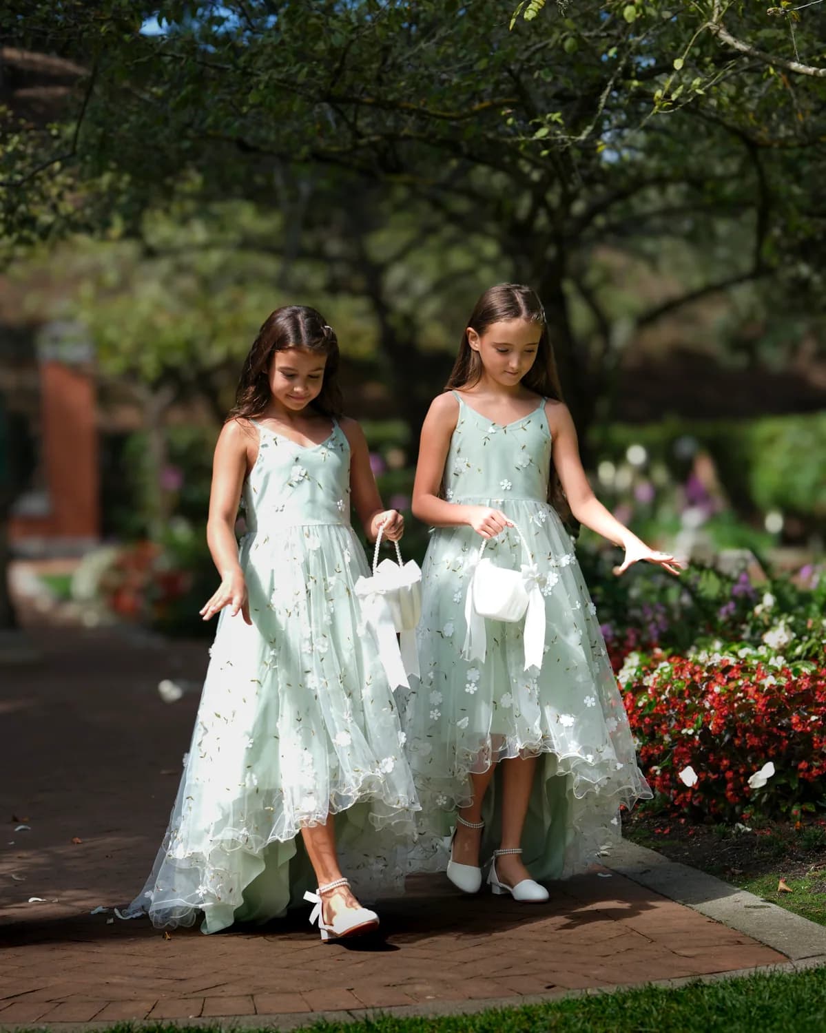 Two flower girls in pale green dresses walking along a garden path