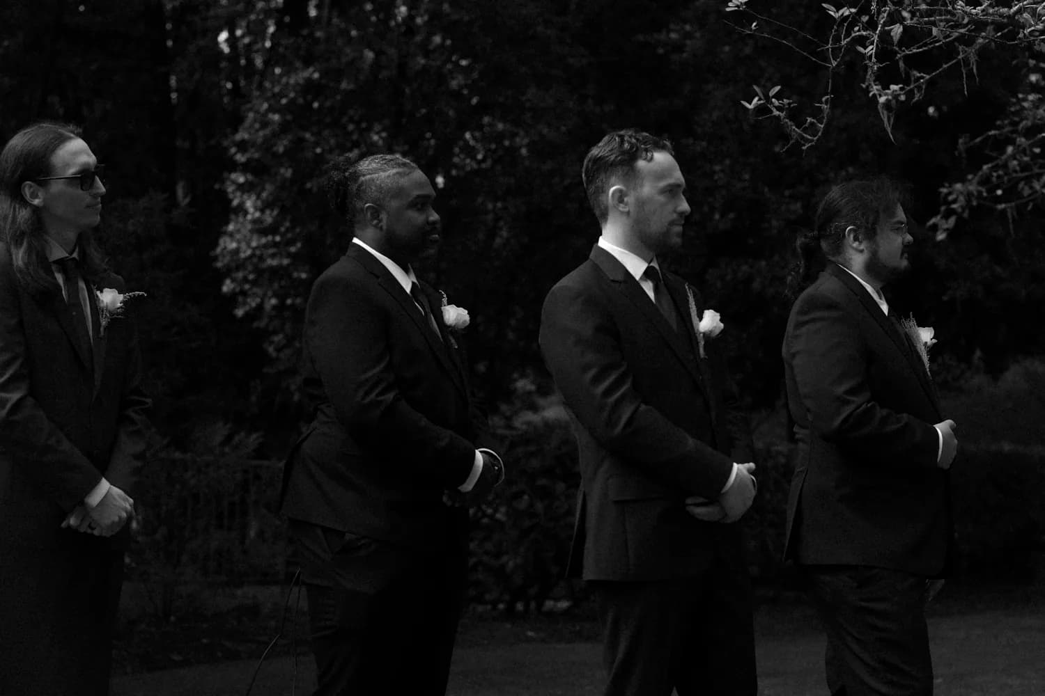 Groomsmen in dark suits watching the ceremony, black and white