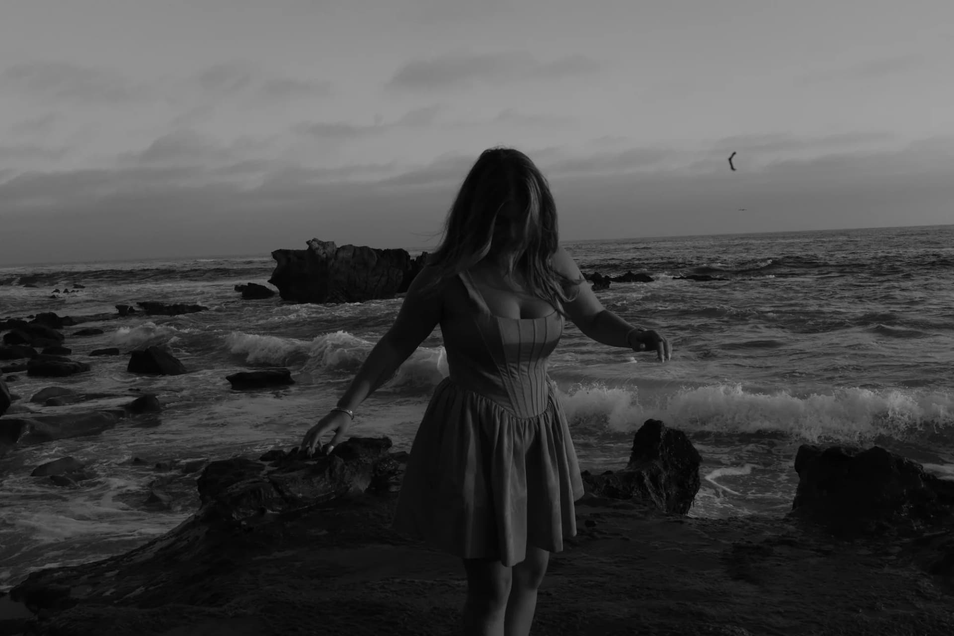 Black and white portrait of a young woman twirling near tide pools on the coast