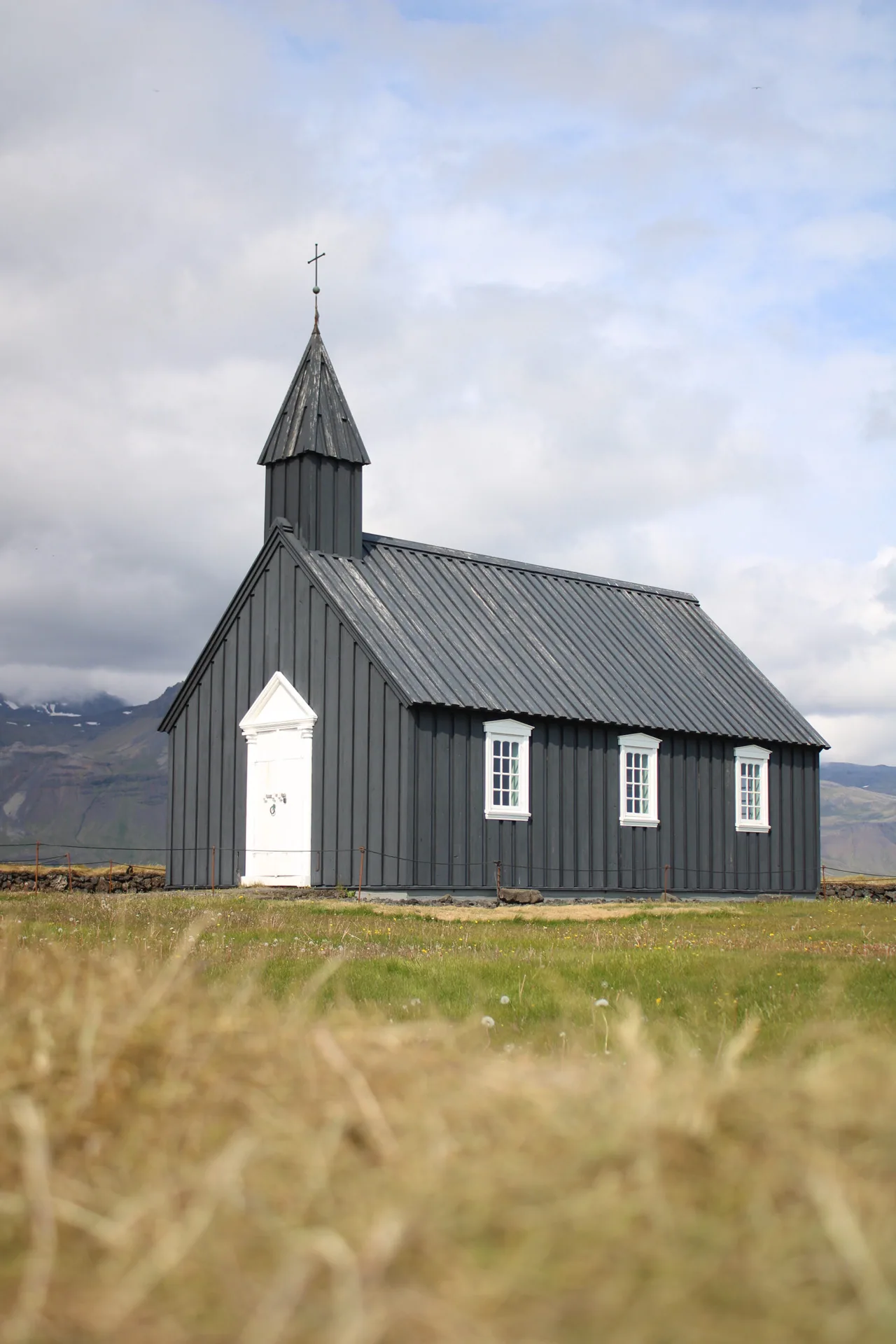 Black wooden church with a white door surrounded by grass and mountains in Iceland
