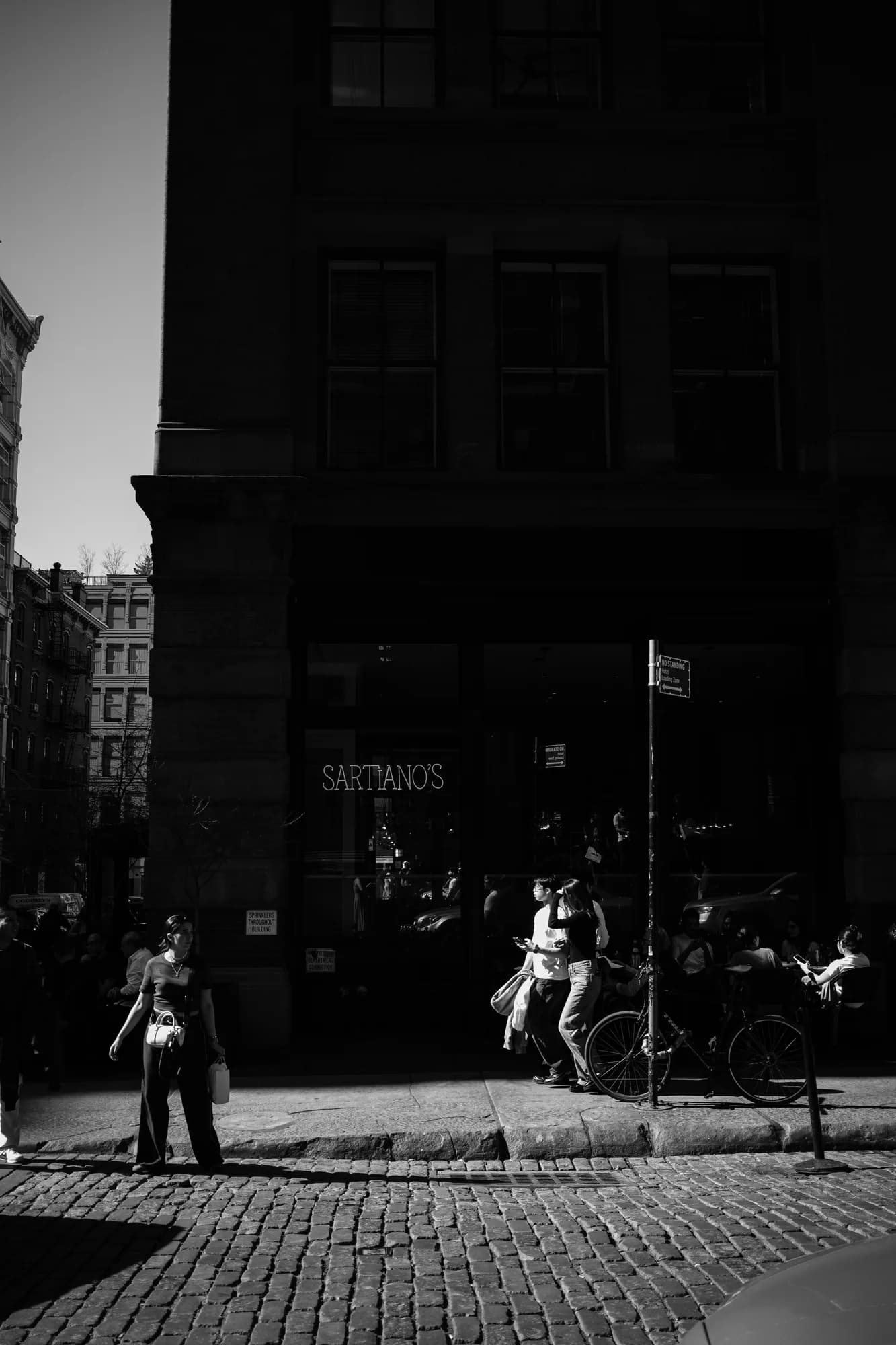 Black and white photo of people on a sunlit New York cobblestone street